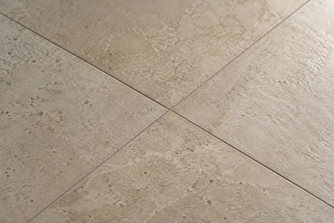 Four warm stone-look porcelain tiles meeting at a grout joint under raking light