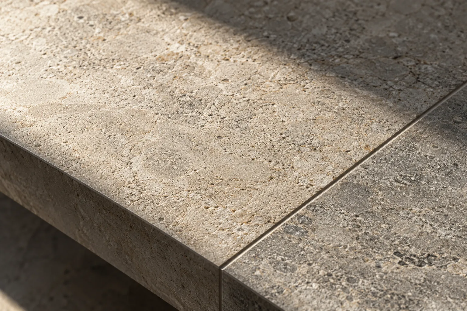 A stone-look surface under low raking light, with a crisp edge and a fine joint between two pieces